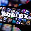 Cellphone held my hand in the dark, screen with many squares game images and the word ROBLOX across