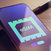 eSIM - Embedded SIM technology concept with smartphone very close lying on a wooden table with esim icon on the screen