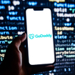 Closeup of smartphone displaying GoDaddy logo with code on a screen in background