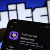 A hand holding a smartphone with the Twitch app open on the screen.