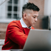 A man in red sitting in front of a laptop.
