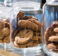 A close up of several chocolate chip cookies in a clear glass jar.