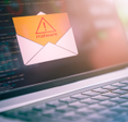 A close-up photo of a laptop with an open envelope icon and a yellow document that says malware coming out of it