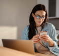 Dark-haired woman with glasses is looking down at her phone with a pleasant expression. 