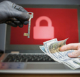 A laptop with a locked screen in the background and a hacker offering a key to unlock encrypted data for money in the foreground.