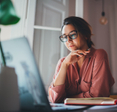 A woman sits at her desk and looks at her laptop. If she&#x27;s using public Wi-Fi, she should check to make sure her VPN is working.