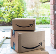Two brown Amazon boxes with the smile logo sit on a front porch. Amazon brushing scams happen when retailers send you unordered packages in hopes to use your info to boost their sales.