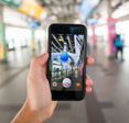 Open public space blurred in the back with hand holding phone screen shows app with game Pokemon GO