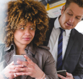 A man is peeking over a woman&#x27;s shoulder at her phone while they are on a bus.