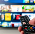 A hand shown holding a remote that&#x27;s pointed at a TV. 