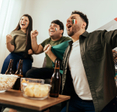 Two men and a woman with face paint and a Mexican flag cheering with beer and popcorn in the living room