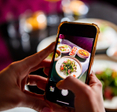 A closeup of a person holding their cell phone to take a photo of food at a restaurant.