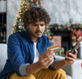 A man is sitting on his couch, holding his phone and his credit card while looking confused.