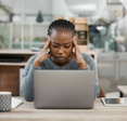 A woman working on her laptop and looking stressed out.
