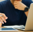 Close-up of a man on his Macbook holding a pen in his hand.