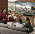 A group of friends in a living room drinking beer and watching a football game on the TV.