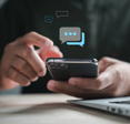 Man using his smartphone while sitting in front of his laptop with abstract text bubbles hovering above the phone.
