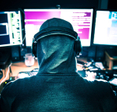 A hooded hacker viewing three computer monitors. 