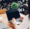 A woman sits at a desk and types on a mac. 