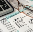 A pair of glasses and the edge of a keyboard are next to a W-4 and a 1040 form. 