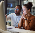 A man and woman sit next to each other and share a computer.  
