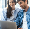 A man and woman sit on the couch while they use a laptop.