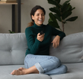 A woman holds a remote while laughing on the couch.