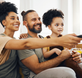 A family of three sits on the couch and watches TV.