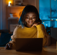 A woman uses her laptop at her table in the evening.