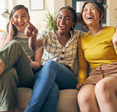 Three friends watch TV and laugh while sitting on the couch.