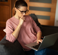 A woman sits on her couch while using her laptop. 