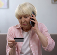 Senior lady looks upset on the phone as she looks at her credit card