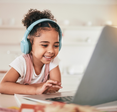 A little girl wears headphones while watching playing on her laptop. 