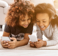 Two children lay on the ground while looking at their phones. 
