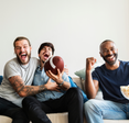 Three men cheer for their football team while watching a game at home.