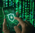 A close-up of a hand holding a smartphone displaying a digital shield with a lock on it, against a green matrix background of binary code.