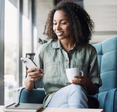 A woman holds a coffee cup and her iPhone.