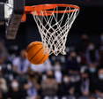 A closeup of a basketball swishing passed the net in a packed stadium