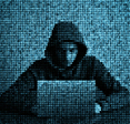 Grainy image of computer code atop hooded hacker using laptop