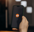 Person holding a phone with the Reddit app loading up on it.