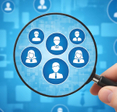 A hand holding a magnifying glass over blue digital user profiles