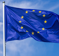 Flag of the European Union waving in the wind on flagpole against the sky with clouds on sunny day.