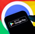 Closeup of a hand holding a smartphone displaying the Google Play Store logo against a Google Chrome background.
