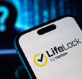 Closeup of LifeLock by Norton logo on smartphone with shady hacker figure in background