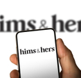 Phone screen with Hims &amp; Hers logo in front of a blurry screen.
