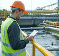 Environmental engineer in a reflective vest inspecting a wastewater treatment plant with a digital tablet.