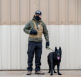 n Immigration and Customs Enforcement (ICE) officer and a black German Shepherd conduct surveillance.