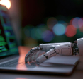 Robotic hand typing on laptop displaying code.