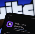 A hand holding a smartphone with the Twitch app open on the screen.