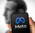 Phone with Meta logo on it in front of faded picture of Mark Zuckerberg.